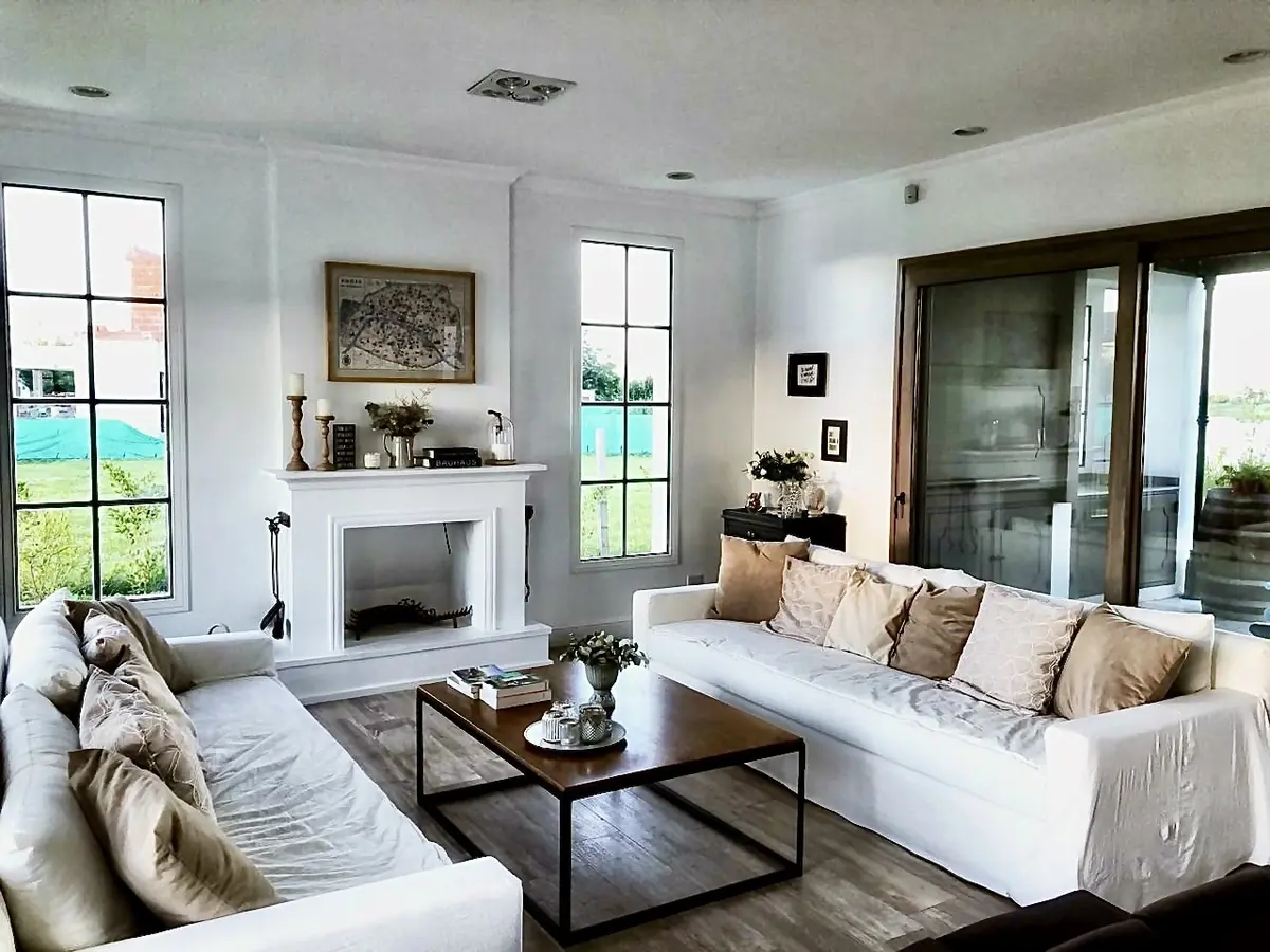 Sala de estar e jantar com janelões, sofá bege e lareira — projeto San Matías, por Marconi Silva Arquitectos, em Belén de Escobar