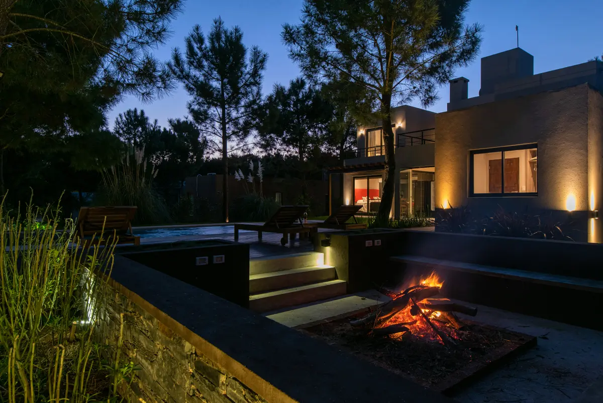 Área externa moderna com lareira e vegetação à noite — projeto Costa Esmeralda 1, por Arquitecto Caceres, em Costa Esmeralda