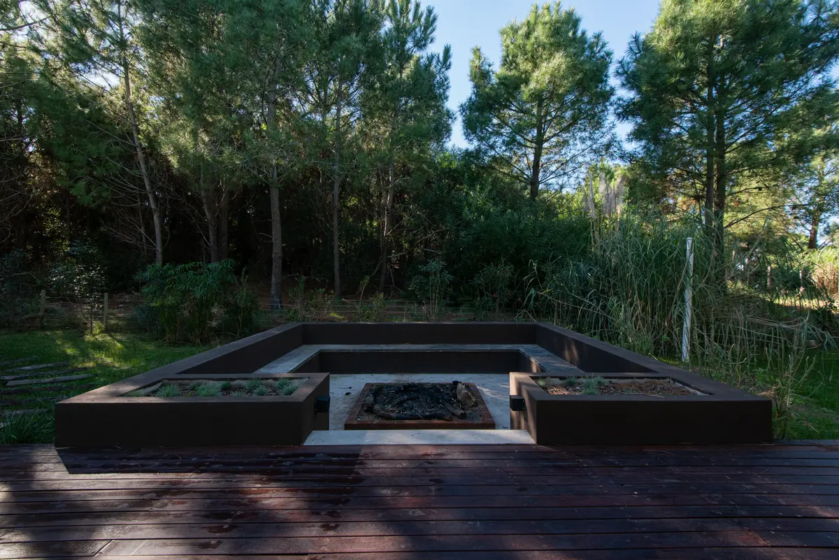 Área externa moderna com churrasqueira embutida e deck de madeira escura — projeto Costa Esmeralda 1, por Arquitecto Caceres, em Costa Esmeralda