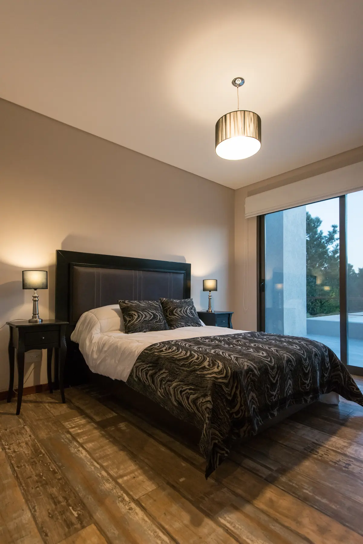 Dormitorio moderno con cama king, luces cálidas y piso de madera — proyecto Costa Esmeralda 2, por Arquitecto Caceres, en Costa Esmeralda