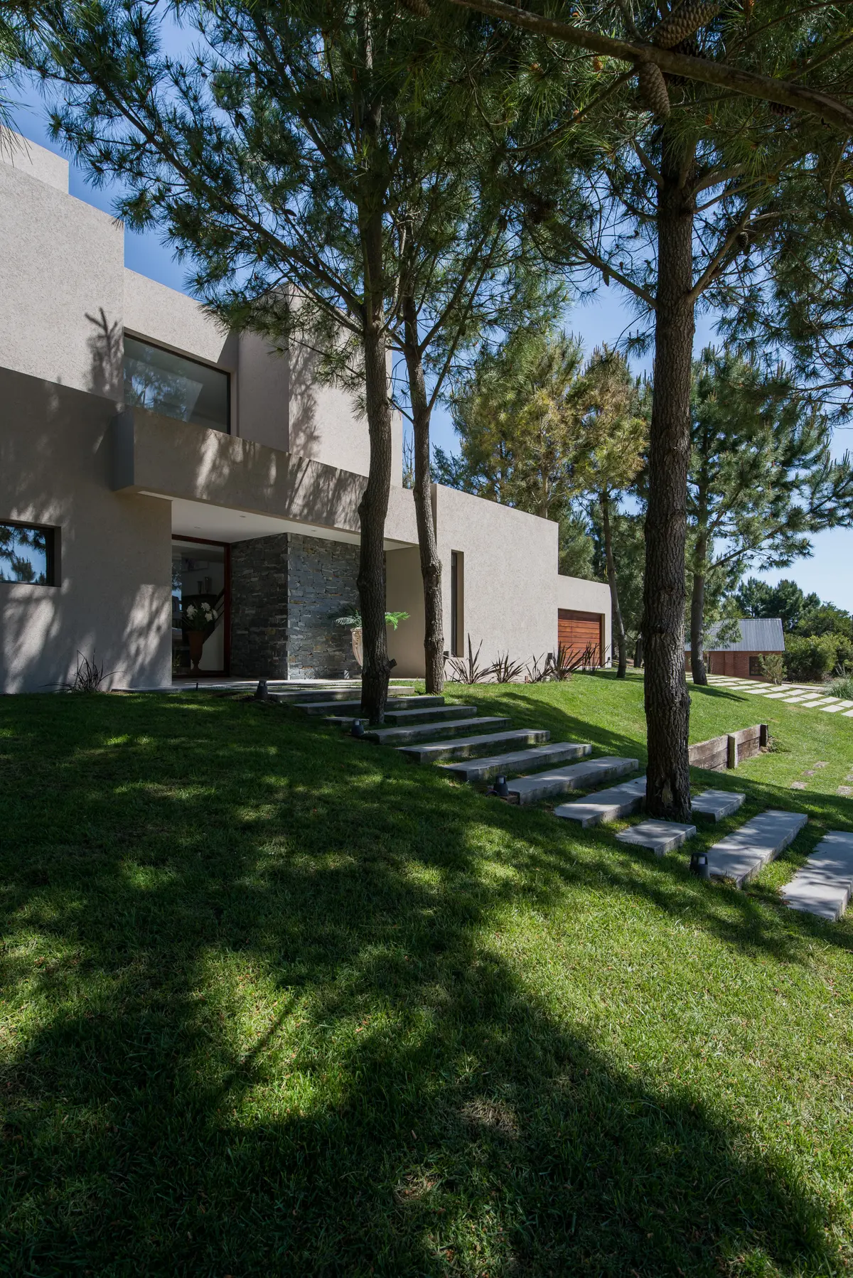 fachada moderna com degraus de pedra e pinheiros — projeto Costa Esmeralda 2, por Arquitecto Caceres, em Costa Esmeralda