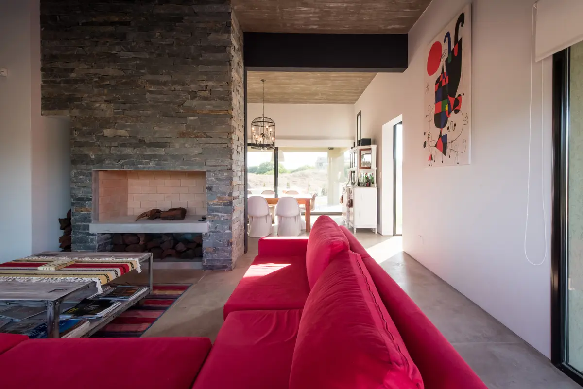 Living moderno con sofá rojo, hogar de piedra y vistas — proyecto Costa Esmeralda 3, por Arquitecto Caceres, en Costa Esmeralda