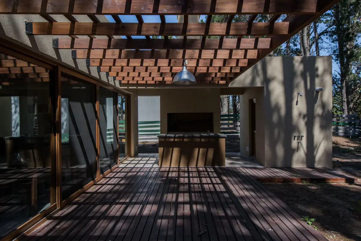 Pátio com deck de madeira, pergolado e churrasqueira — projeto Costa Esmeralda Casa MAI Lote 374 Deportiva, por Arquitecto Caceres, em Costa Esmeralda