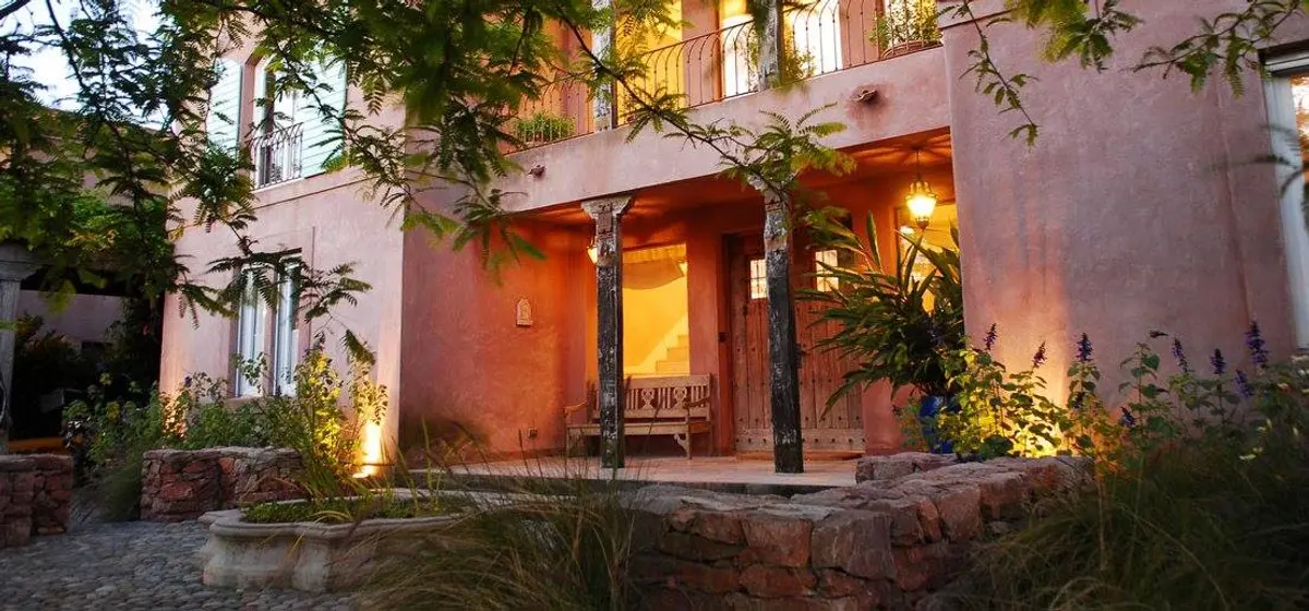 Fachada rústica mediterrânea com vegetação exuberante e iluminação quente — projeto Laguna del Sol, por Estudio Moreto Bensusan, em Tigre