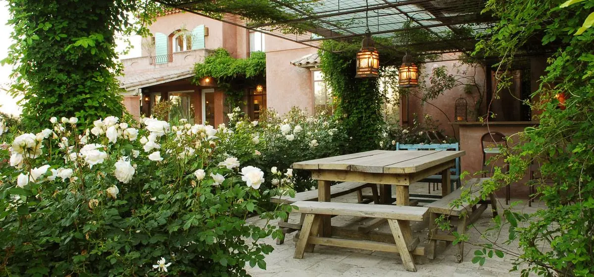 Pátio rústico com flores brancas, mesa de madeira e pérgola — projeto Laguna del Sol, por Estudio Moreto Bensusan, em Tigre