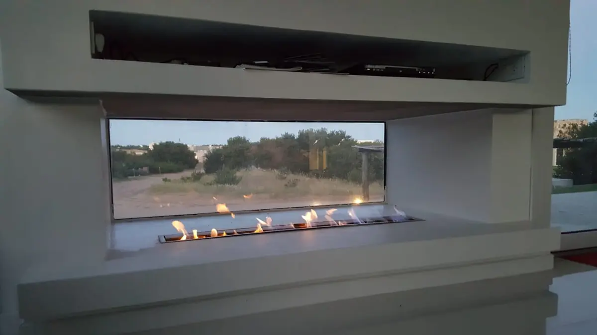 Living con hogar lineal y gran ventanal al campo — proyecto Costa Esmeralda, por Cuello Selva, en Costa Esmeralda