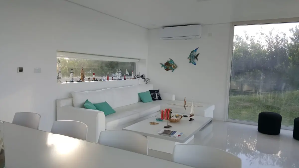 Living moderno minimalista con sofá blanco y grandes ventanales — proyecto Costa Esmeralda, por Cuello Selva, en Costa Esmeralda