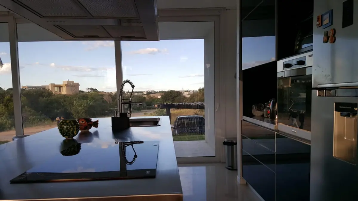 Cocina moderna con isla grande y vista a jardín — proyecto Costa Esmeralda, por Cuello Selva, en Costa Esmeralda