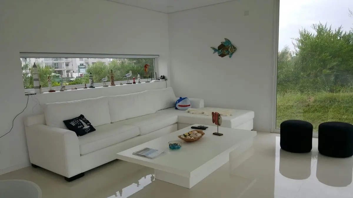 Living moderno minimalista con grandes ventanales y vista verde — proyecto Costa Esmeralda, por Cuello Selva, en Costa Esmeralda