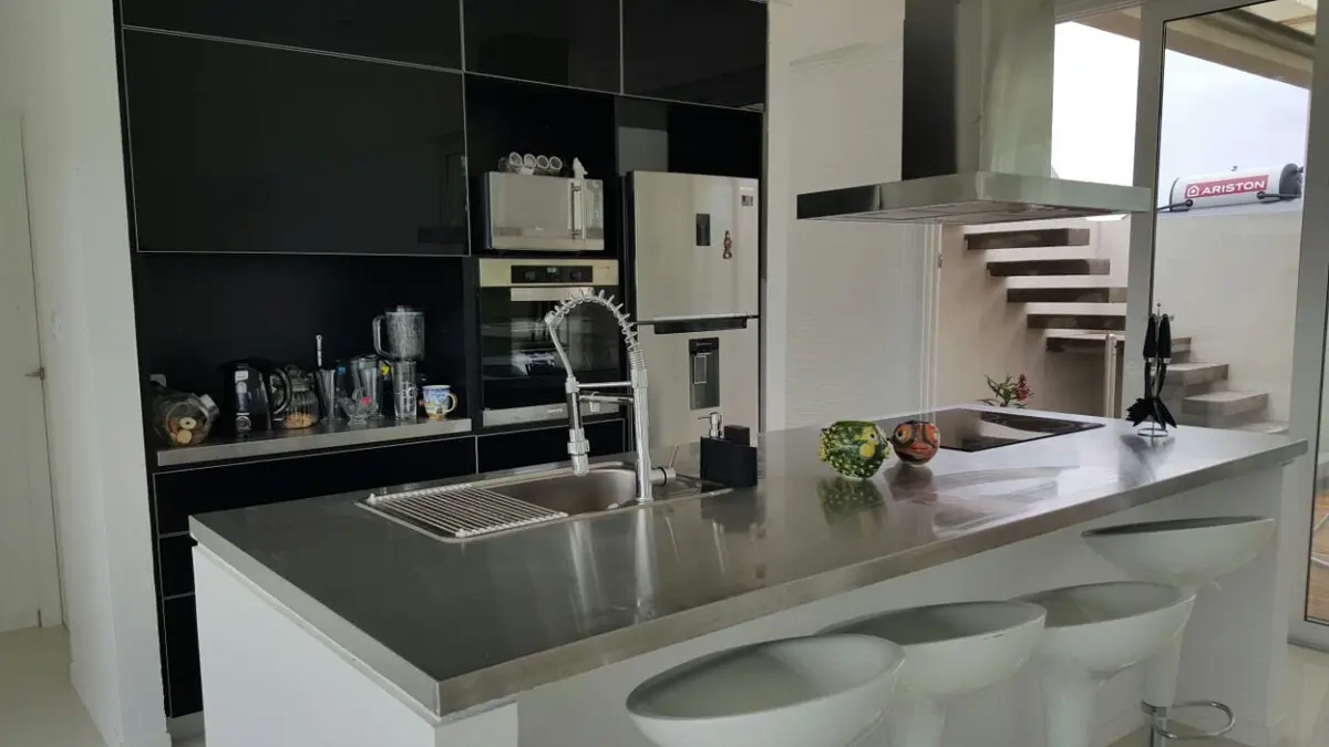 Cocina moderna con gabinetes negros y mesada de acero inoxidable — proyecto Costa Esmeralda, por Cuello Selva, en Costa Esmeralda