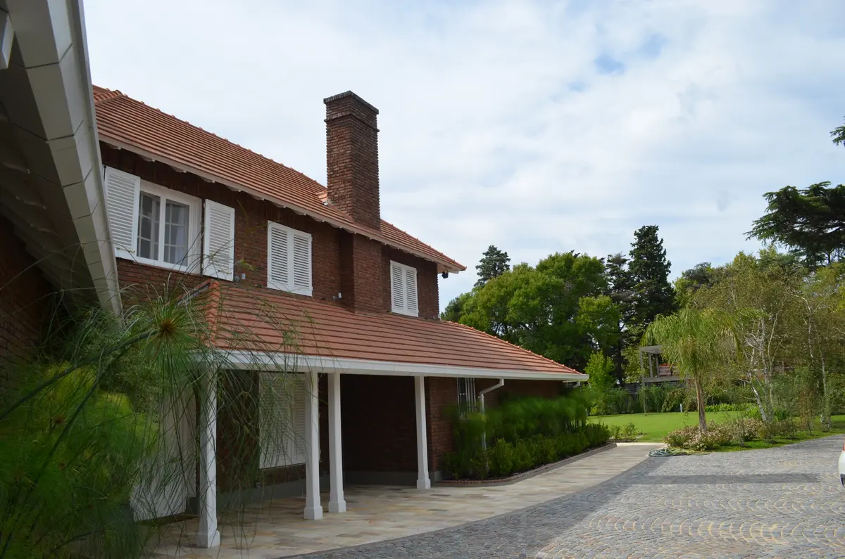fachada de tijolos aparentes com vegetação exuberante — projeto Casa en Barrio El Jockey - San Isidro, por GEN STUDIO  COMOTTO - SOMMER, em San Isidro
