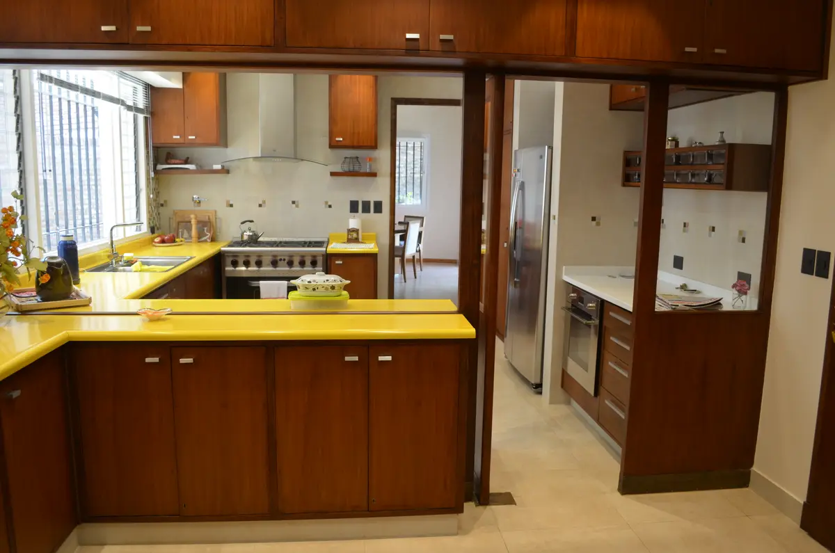 Cocina moderna con muebles de madera oscura y encimera amarilla — proyecto Casa en Barrio El Jockey - San Isidro, por GEN STUDIO  COMOTTO - SOMMER , en San Isidro
