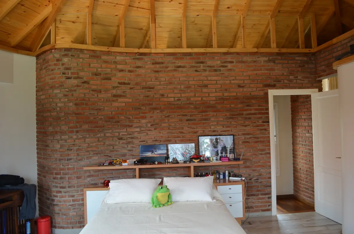 Dormitorio con pared curva de ladrillo expuesto y vigas de madera — proyecto Casa en Barrio El Jockey - San Isidro, por GEN STUDIO  COMOTTO - SOMMER , en San Isidro