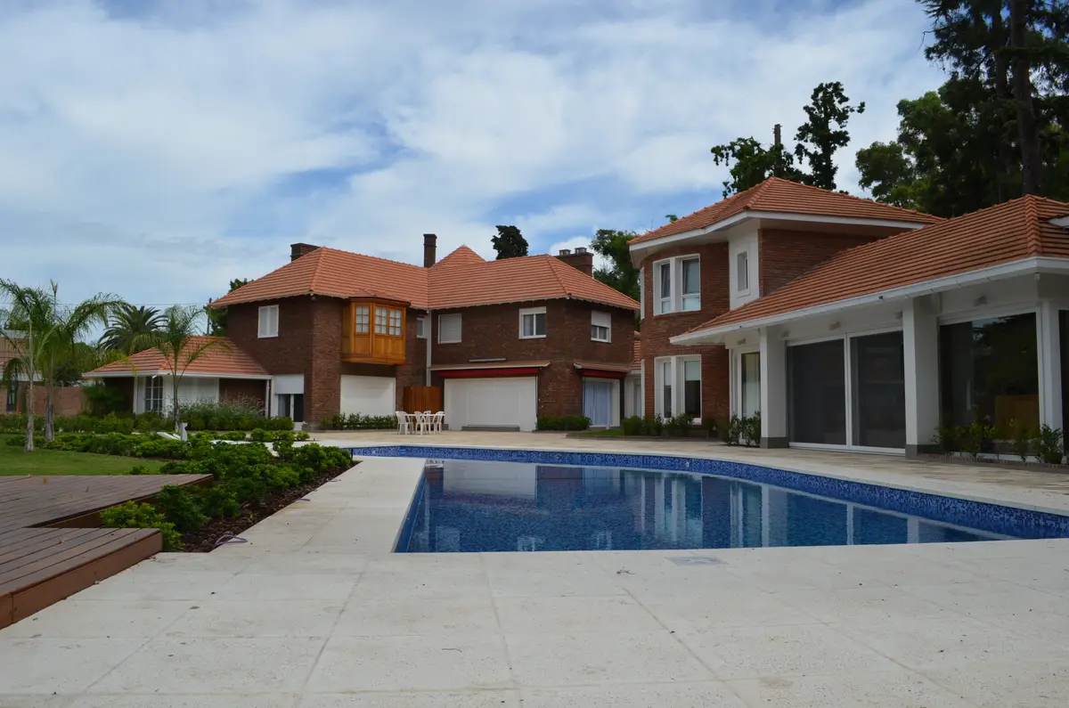 Ampla área de piscina com casas de tijolos e telhados vermelhos — projeto Casa en Barrio El Jockey - San Isidro, por GEN STUDIO  COMOTTO - SOMMER, em San Isidro