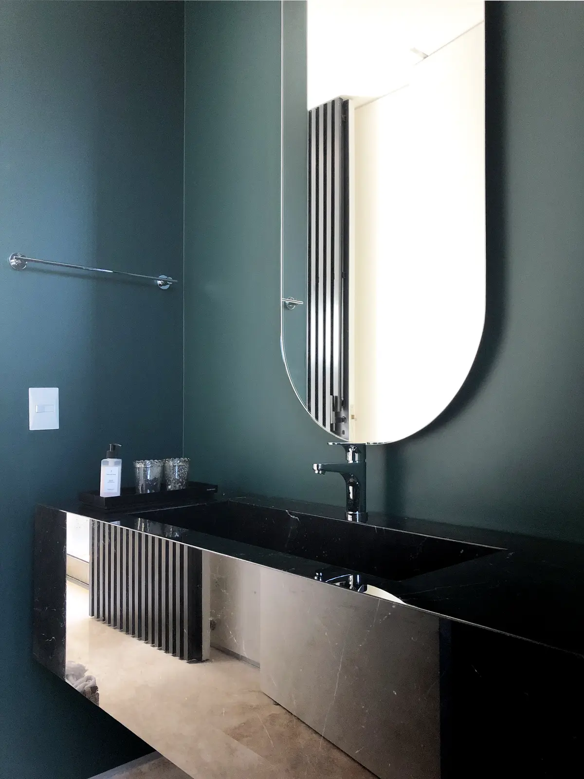 baño moderno con paredes verde oscuro, mesada de piedra negra y espejo ovalado — proyecto Las Lomas , por Estudio MMS , en San Isidro