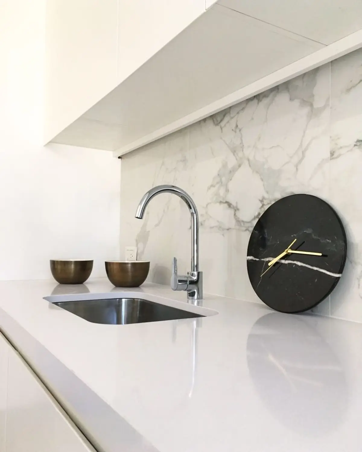 Cocina moderna con mesada blanca, bacha acero y reloj decorativo — proyecto Kennedy, por JT ARQUITECTURA, en CABA