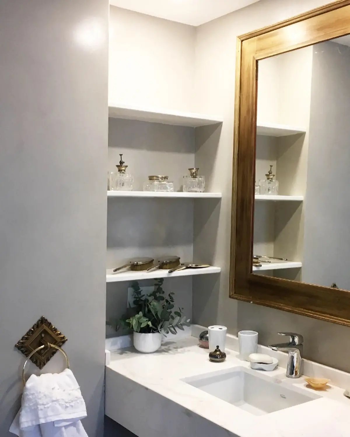 Baño con espejo dorado grande, nicho de estanterías empotradas y encimera de mármol — proyecto Arenales, por JT ARQUITECTURA, en CABA