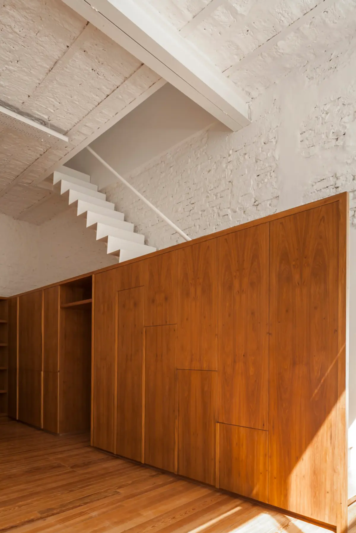 Habitación moderna con amplios armarios de madera y escalera flotante — proyecto PH Tamborini , por ariana werber arquitecta, en Núñez
