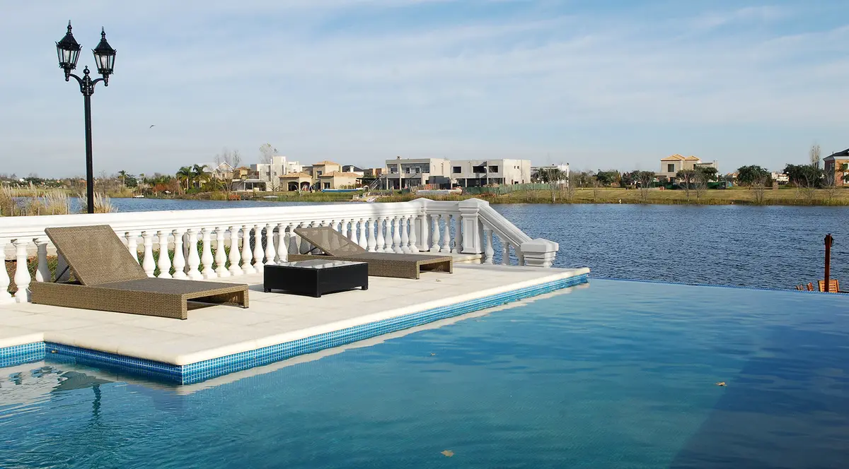 Pileta infinita con reposeras y balcón con vista al agua — proyecto San Isidro Labrador, por ARQCONS, en San Isidro