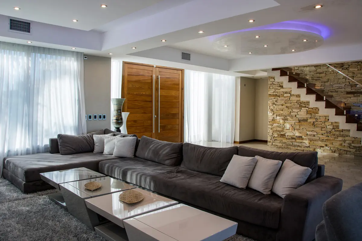 Living moderno con sofá grande y luz abstracta — proyecto La Reserva Cardales I, por ARQCONS, en Los Cardales