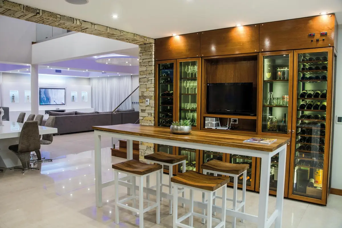 Living moderno con cava de vinos integrada y barra alta — proyecto La Reserva Cardales I, por ARQCONS, en Los Cardales