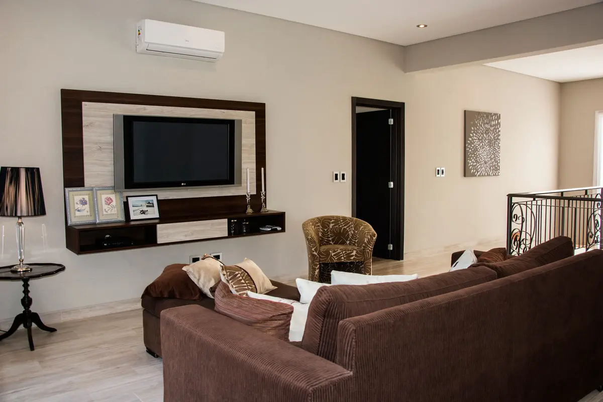 Sala de estar moderna con sofá marrón en forma de U y sillón de ratán — proyecto Casa Reserva Cardales II, por ARQCONS, en Los Cardales