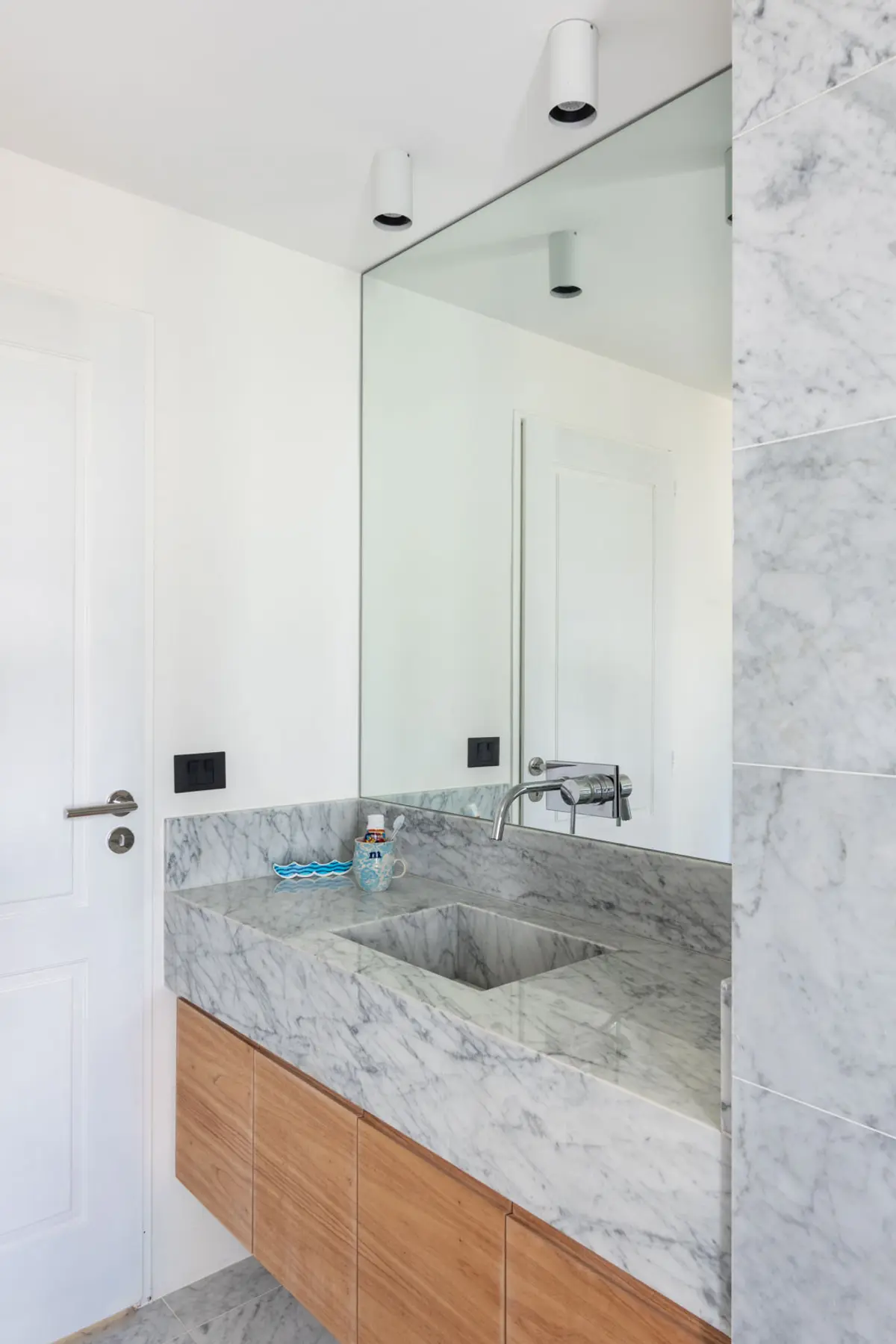 Baño moderno con mesada de mármol, muebles flotantes de madera y gran espejo — proyecto Boating I, por Estudio Arq. Ana M. Carrera, en Boating Club
