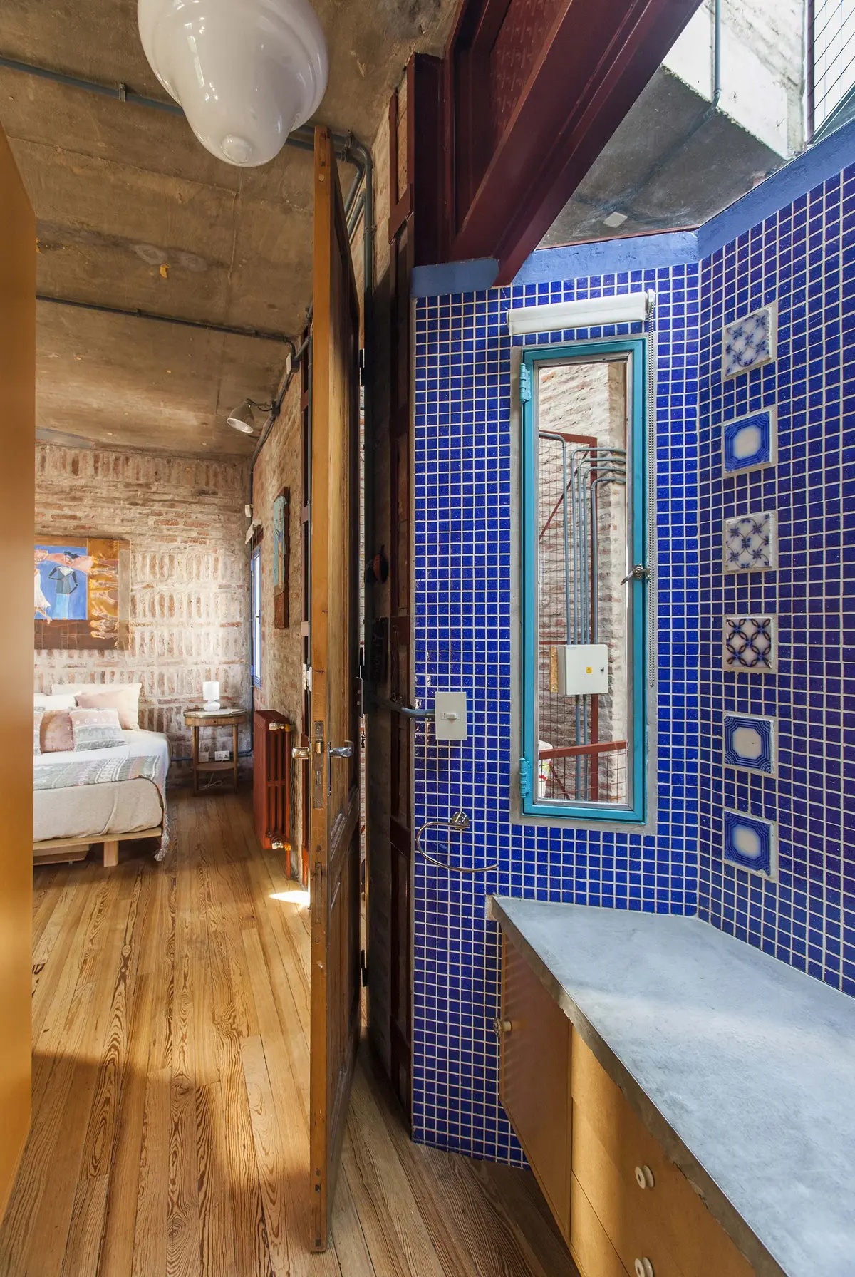 Corredor industrial com azulejos azuis e piso de madeira — projeto Casa Warnes, por Silvia Soqueff, em CABA