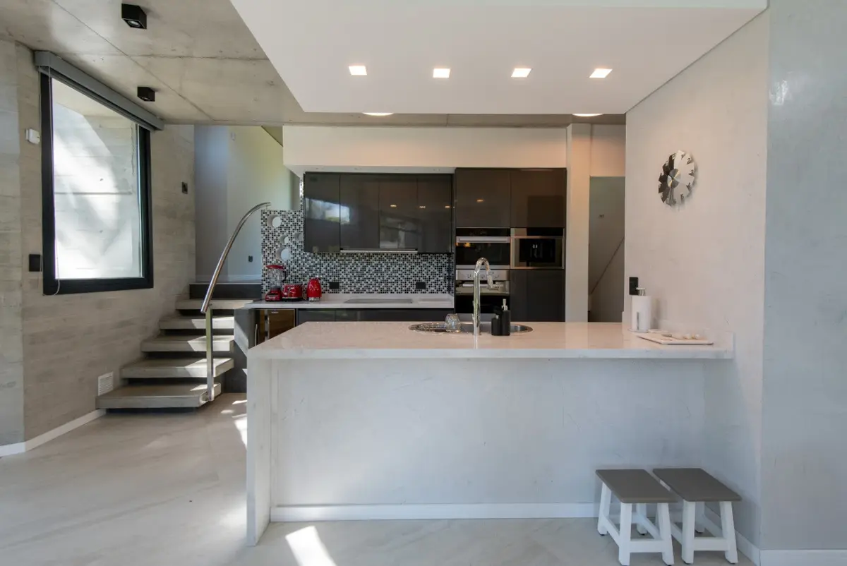 Cocina moderna con isla y paredes de hormigón — proyecto Casa G y G, por TAVA Coop, en Cariló
