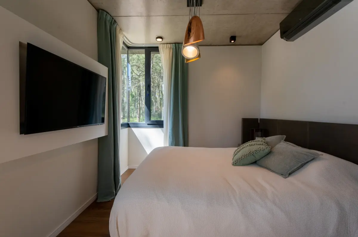 Quarto moderno com cama grande, pendentes e cortinas azuis — projeto Casa G y G, por TAVA Coop, em Cariló