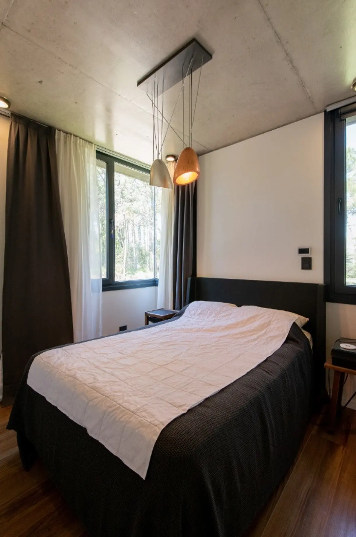 Quarto moderno com teto de concreto aparente e vista para floresta — projeto Casa G y G, por TAVA Coop, em Cariló