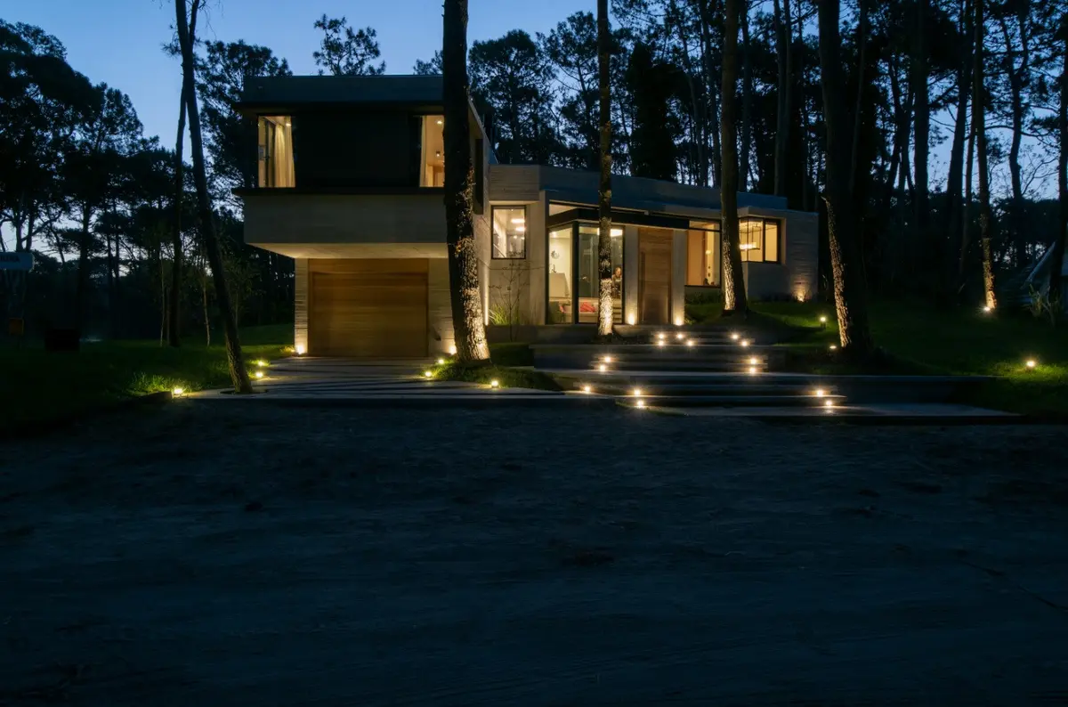fachada moderna de concreto e madeira iluminada na floresta — projeto Casa G y G, por TAVA Coop, em Cariló