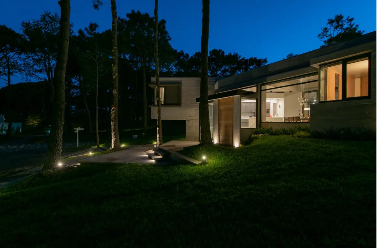fachada moderna de concreto e madeira em floresta com iluminação quente — projeto Casa G y G, por TAVA Coop, em Cariló