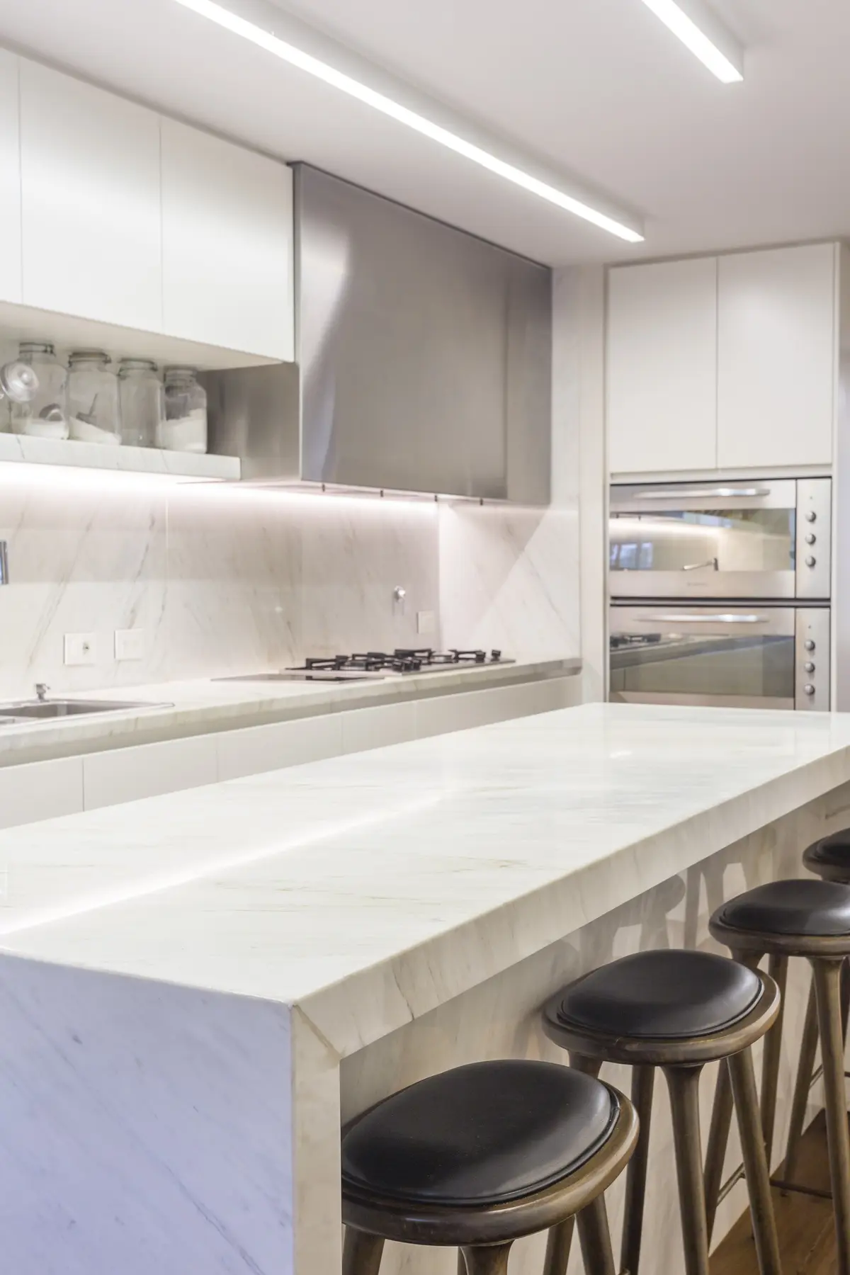 Cocina minimalista blanca con isla de mármol y taburetes negros — proyecto The Classic, por BAS Y GARCIA , en San Isidro