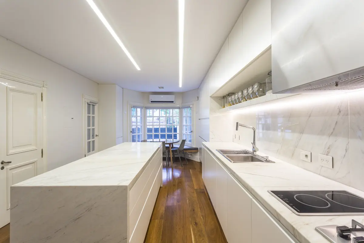 Cocina minimalista blanca con isla central y vista urbana — proyecto The Classic, por BAS Y GARCIA , en San Isidro