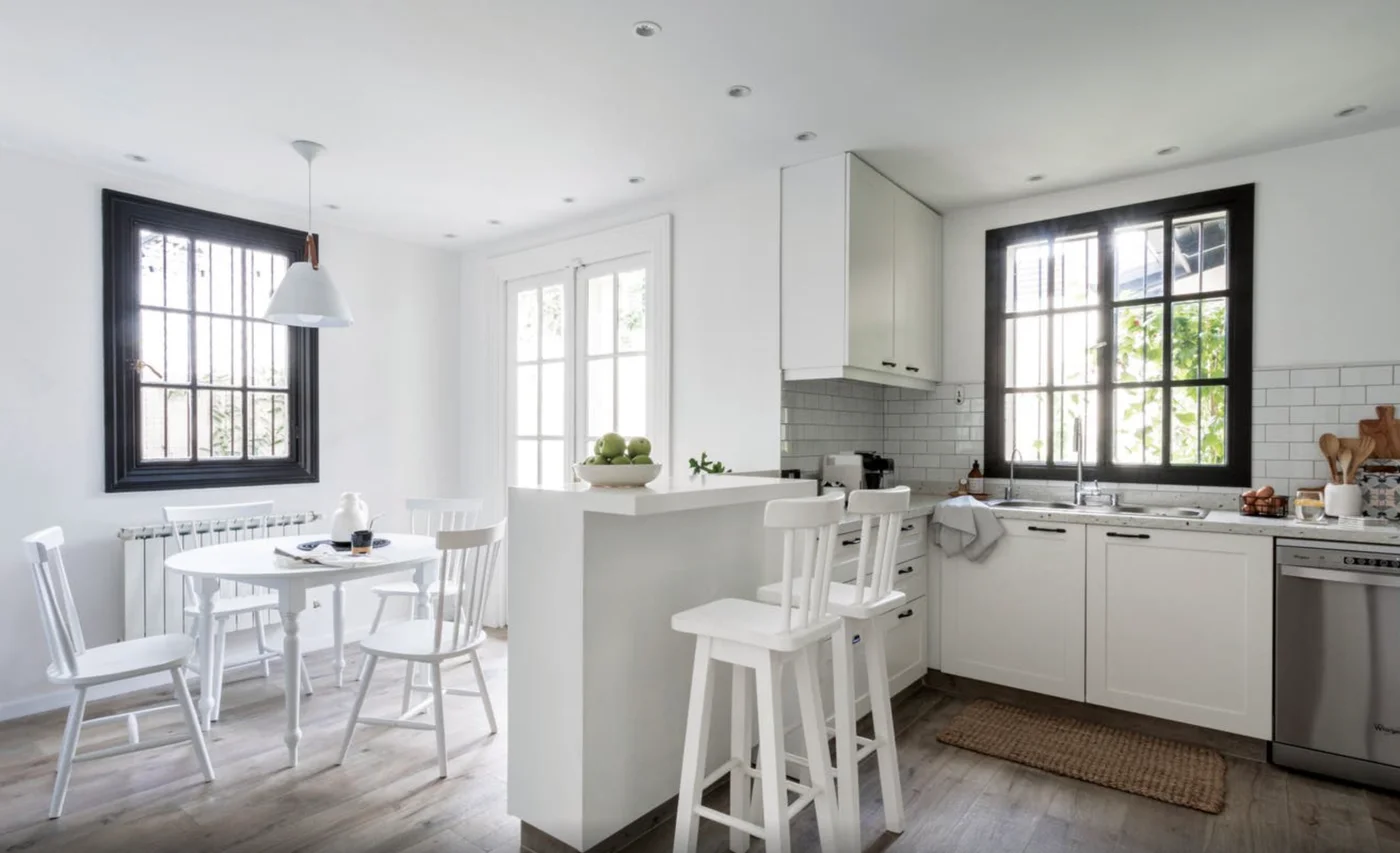 Cocina blanca moderna con isla, grandes ventanales y comedor integrado