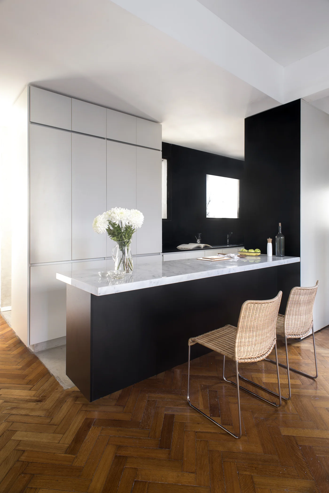 Cocina minimalista con isla central, mesada de mármol y muebles blancos.