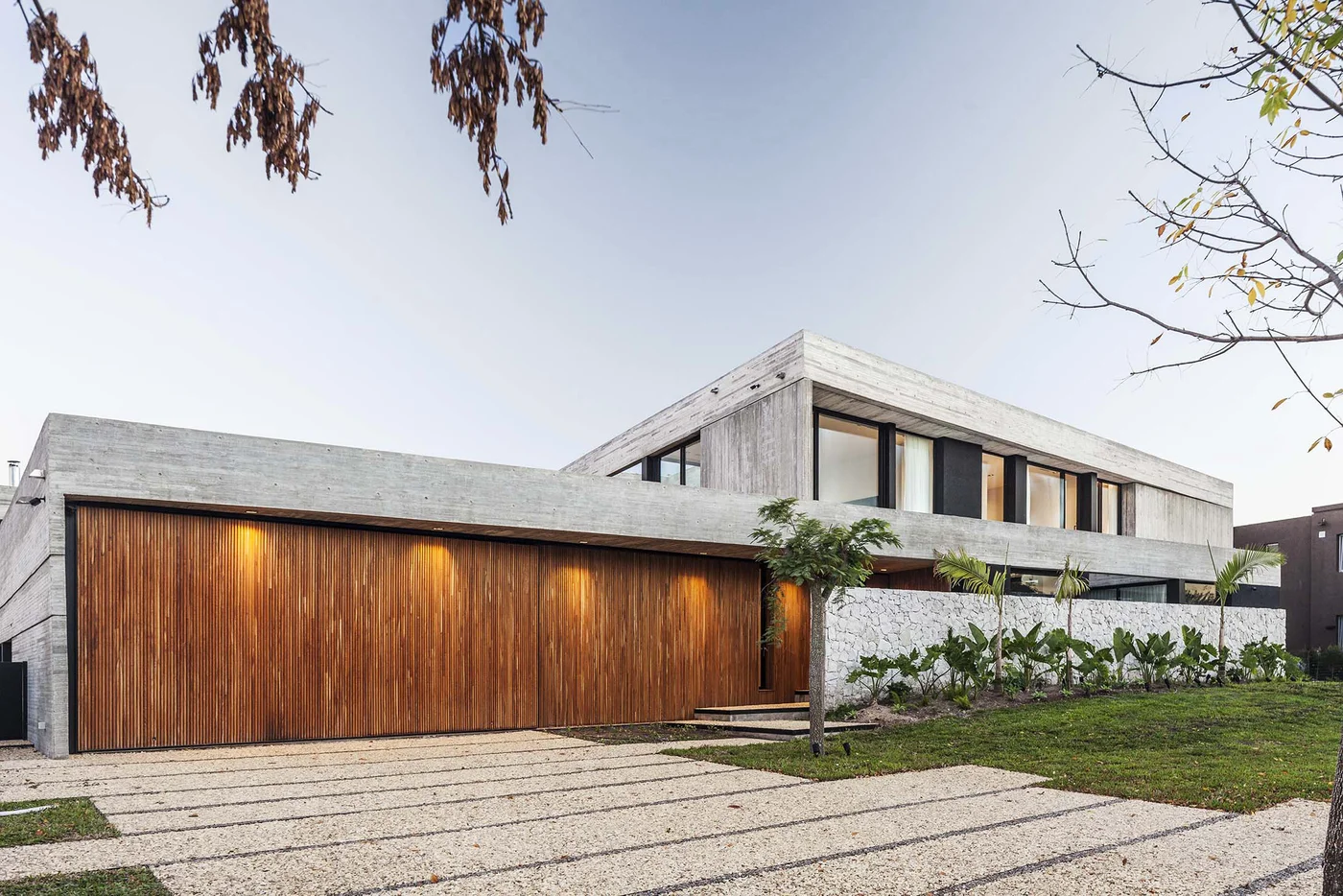 Casa moderna de hormigón y madera con deck y jardín frontal.