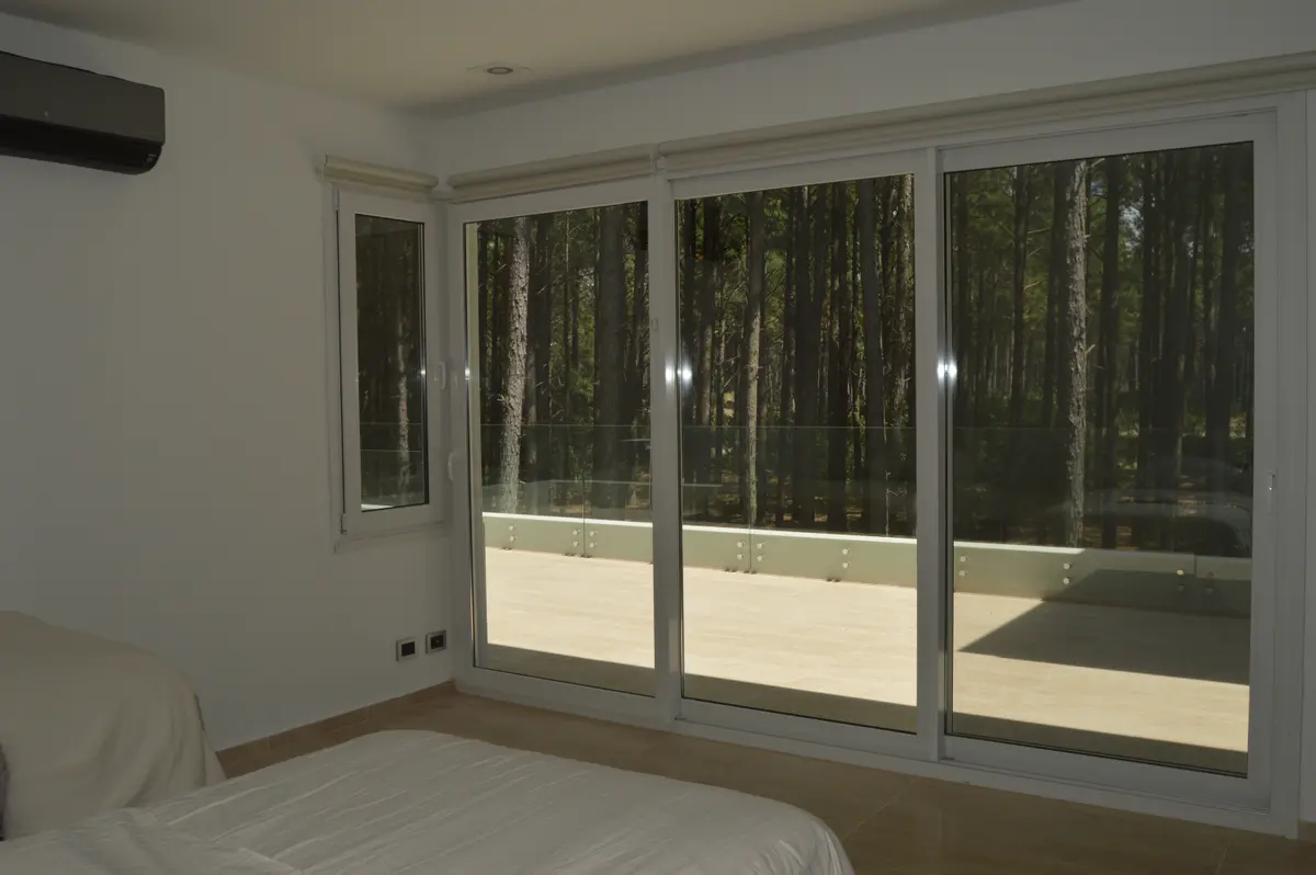 Dormitorio moderno con vista a bosque y puerta corrediza de vidrio — proyecto PINAMAR NORTE, por LADAGA-RUARTE-Pinamar, en Pinamar