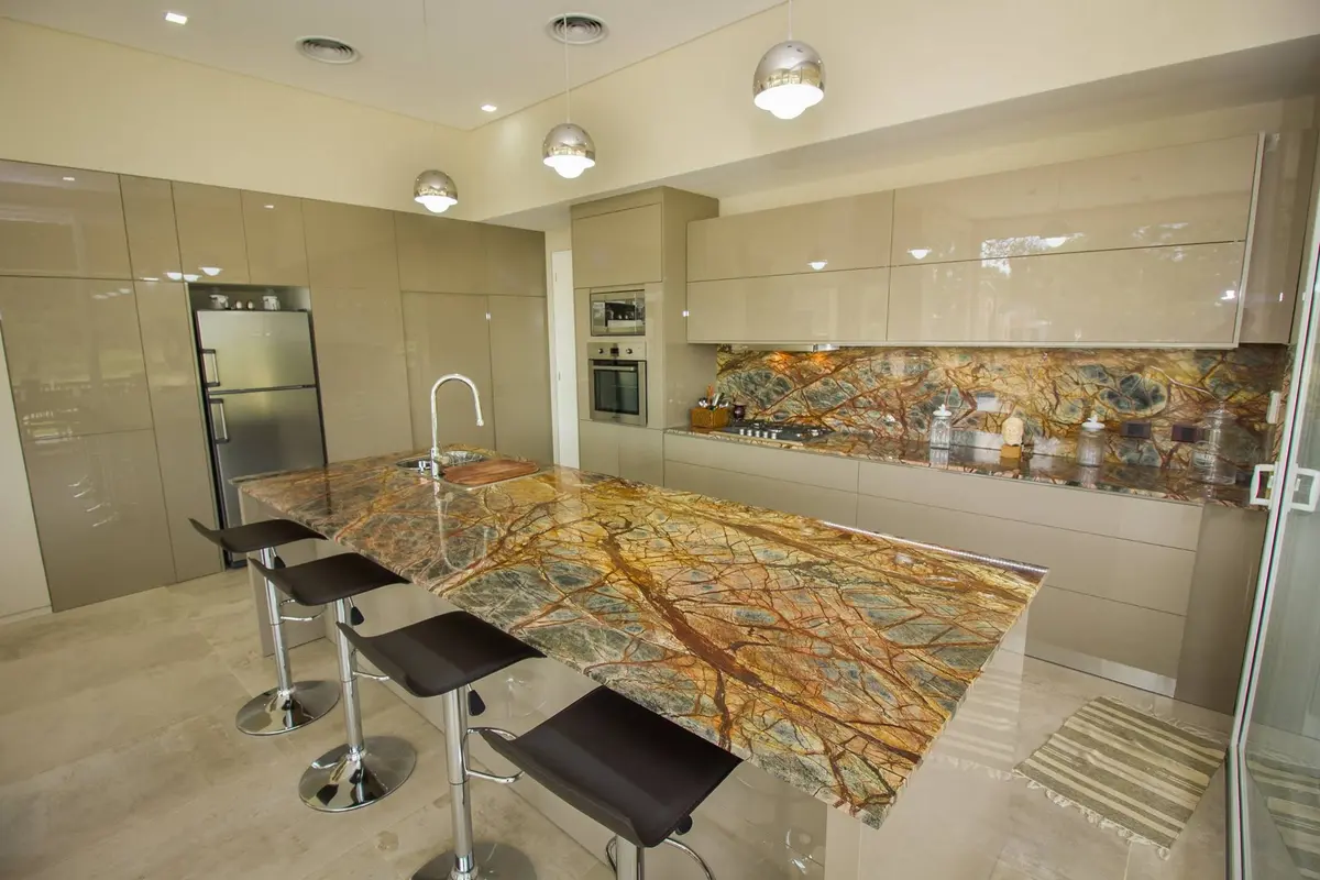 cocina moderna con isla de piedra llamativa y gabinetes brillantes — proyecto LA HERRADURA - Boulevard III, por LADAGA-RUARTE-Pinamar, en Pinamar