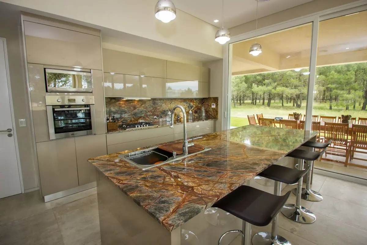 Cocina moderna con isla de piedra espectacular y vistas al bosque — proyecto LA HERRADURA - Boulevard III, por LADAGA-RUARTE-Pinamar, en Pinamar