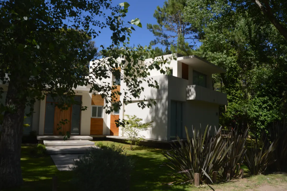 Fachada moderna con hormigón visto, ventanas amplias y vegetación exuberante — proyecto CARILO - Boyero, por LADAGA-RUARTE-Pinamar, en Cariló