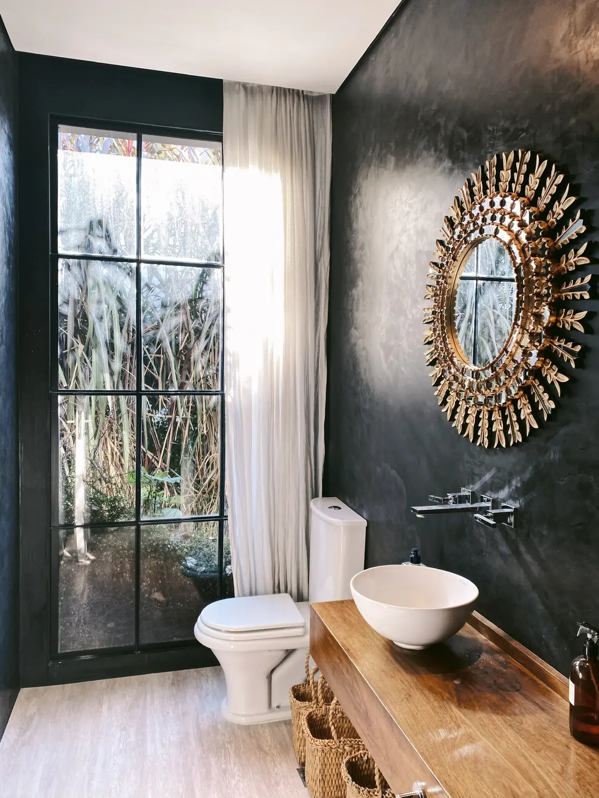baño con espejo sol, ventana grande y paredes oscuras texturizadas — proyecto Ayres del Pilar, por Detry Miguens Arquitectura, en Pilar