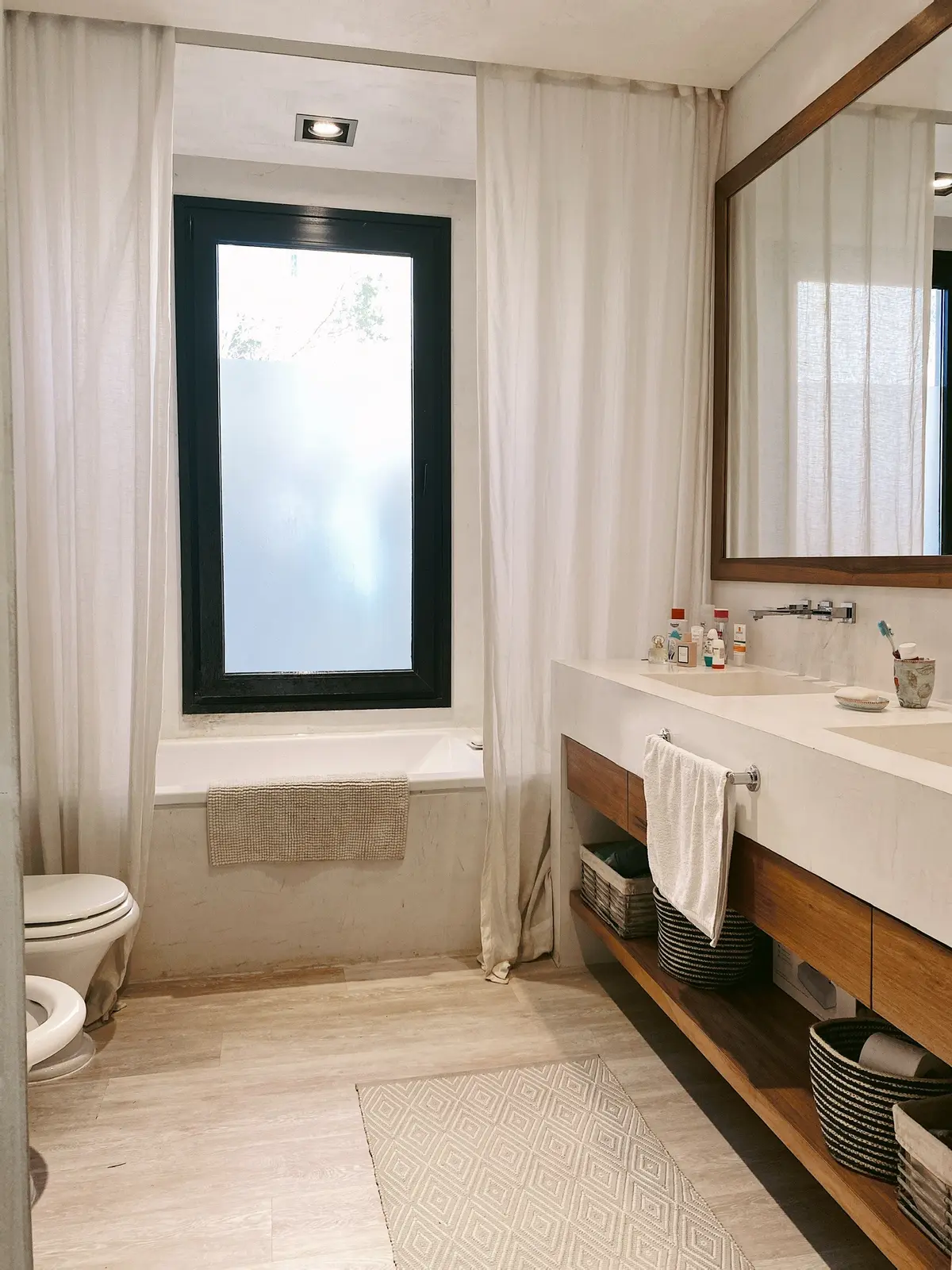 Baño moderno escandinavo con ventana grande y tocador de madera — proyecto Ayres del Pilar, por Detry Miguens Arquitectura, en Pilar