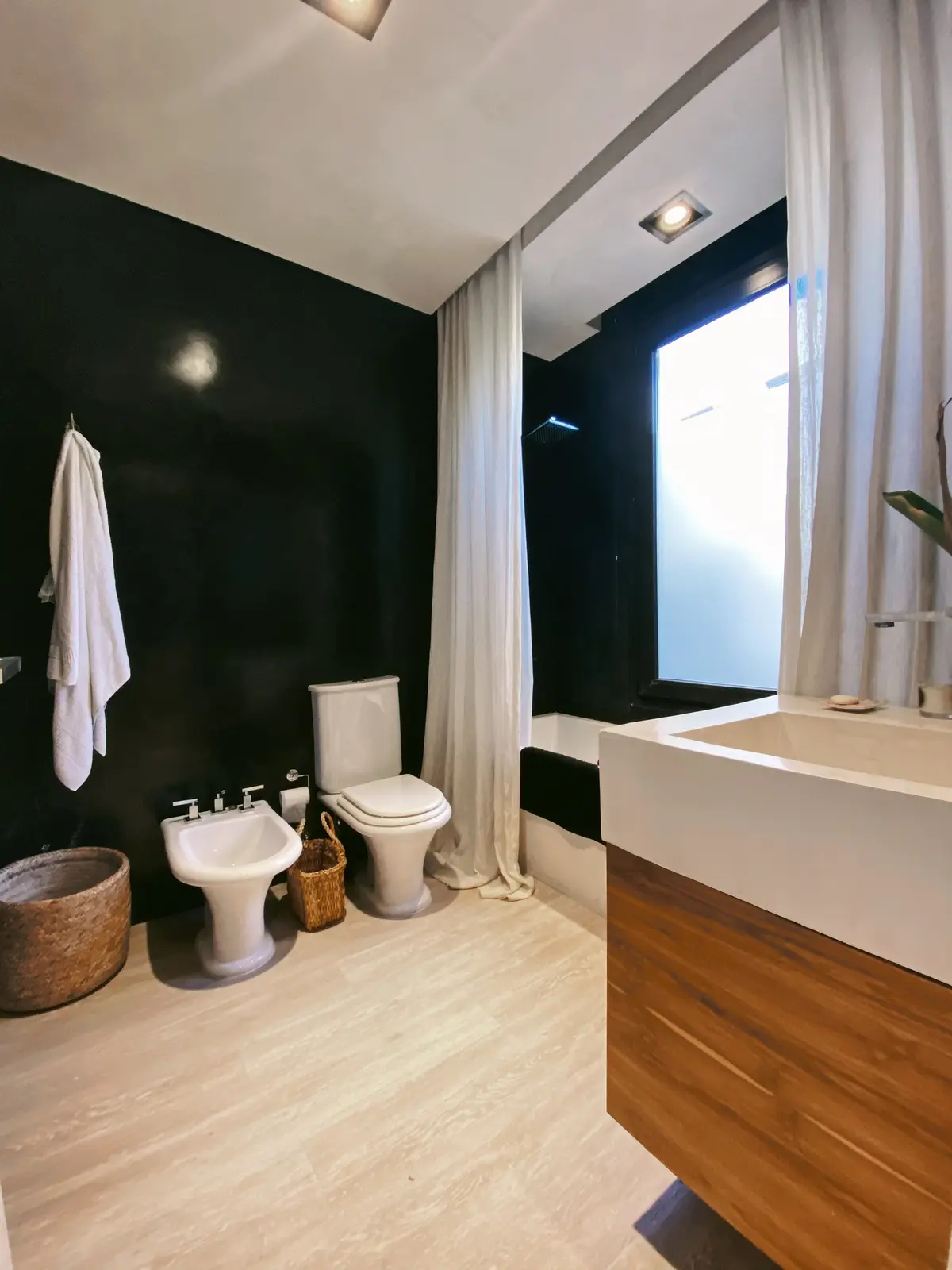 Baño moderno con paredes negras, bidet, bañera y ventana — proyecto Ayres del Pilar, por Detry Miguens Arquitectura, en Pilar