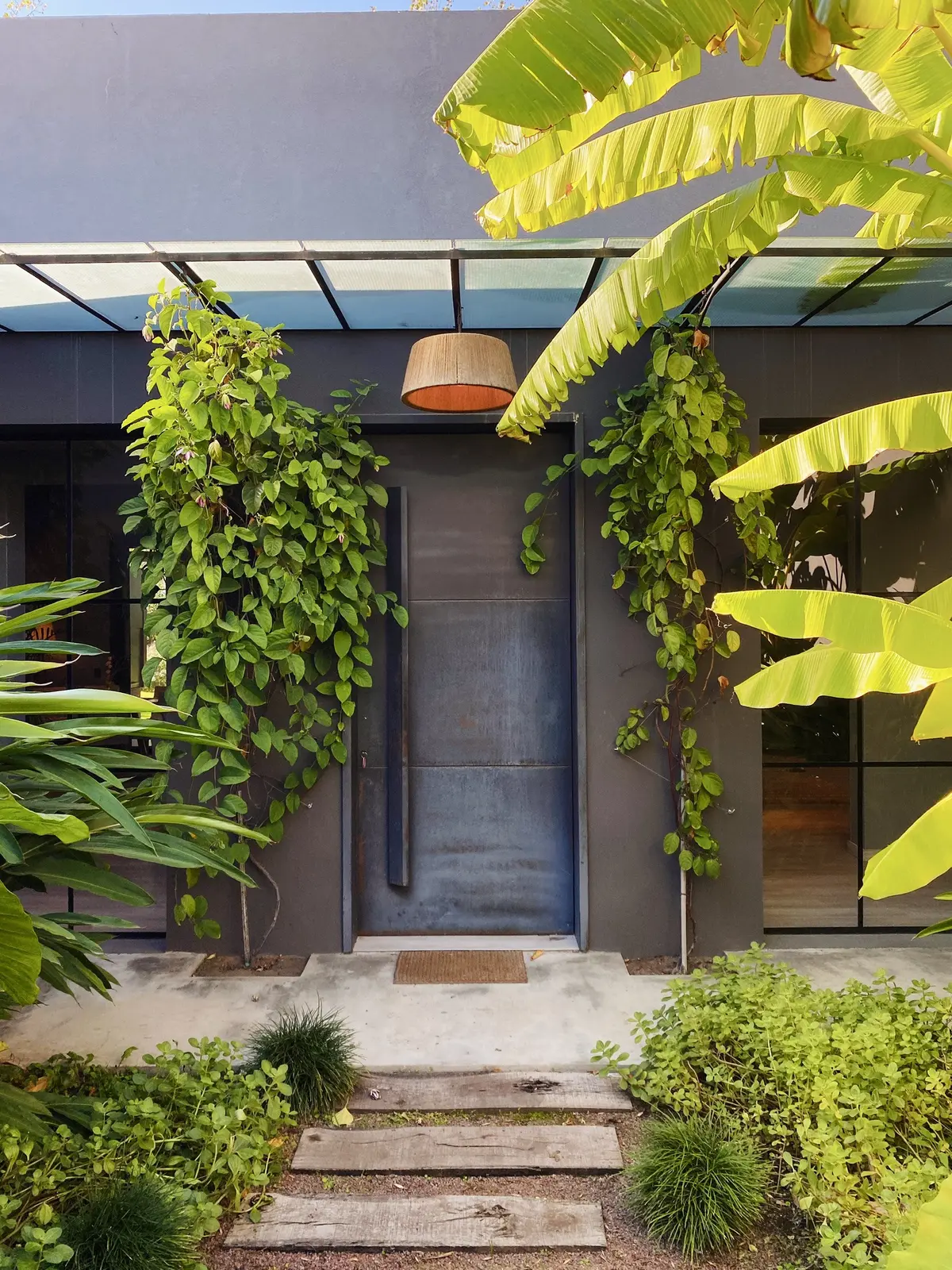 Fachada moderna con muro verde exuberante y puerta industrial — proyecto Ayres del Pilar, por Detry Miguens Arquitectura, en Pilar