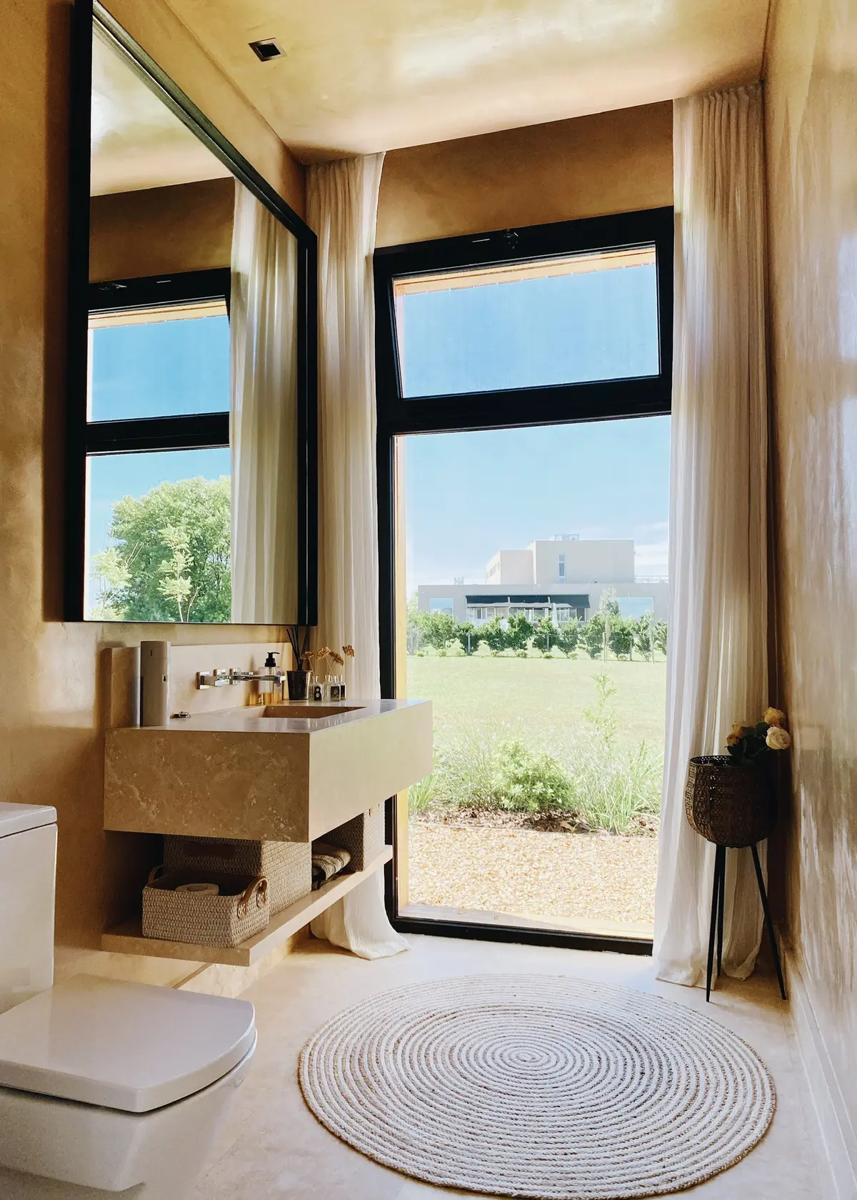 Baño moderno con grandes ventanales, lavabo de piedra y vista al campo — proyecto Pilará 38, por Detry Miguens Arquitectura, en Pilará