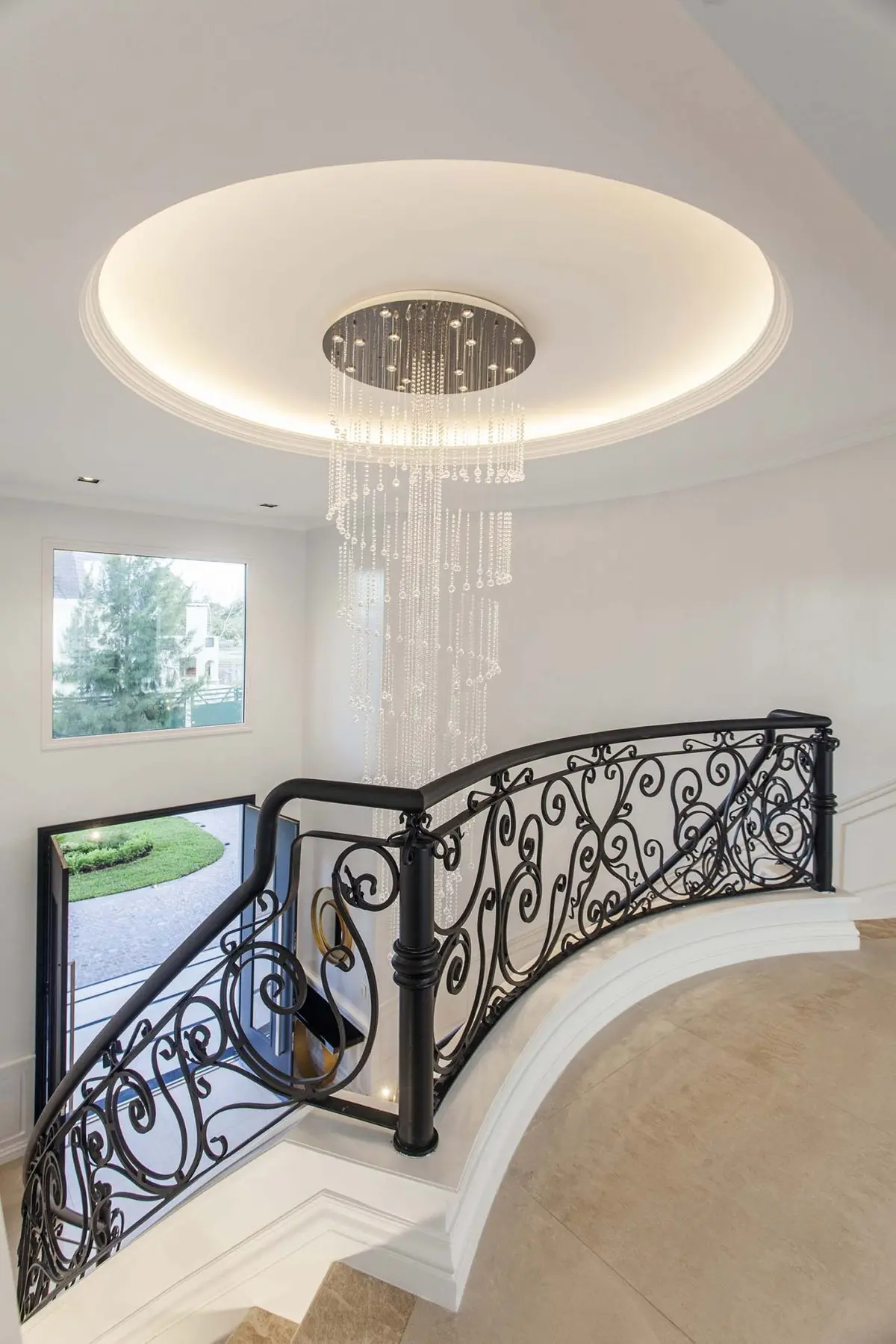 Escada moderna de pé-direito duplo com lustre de cristal e corrimão ornamentado — projeto DD House, por A+R Arquitectos
