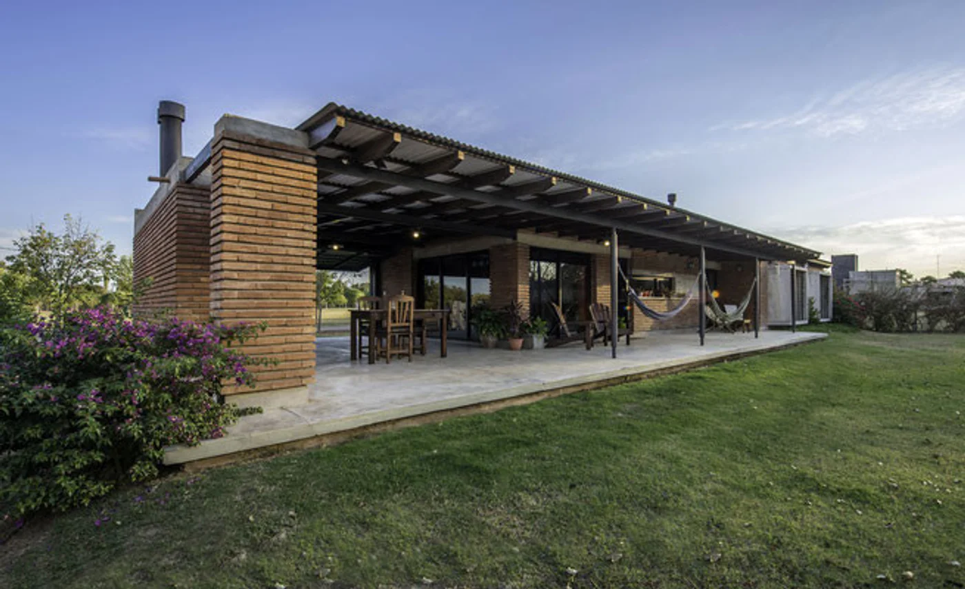 Fachada moderna rústica con pérgola de ladrillos y césped