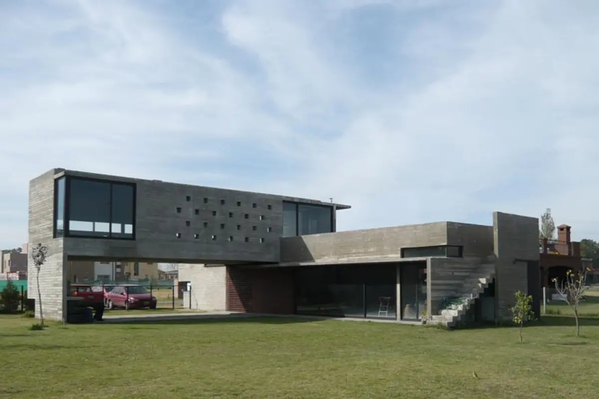Casa contemporánea con fachada de hormigón y ladrillo, amplio jardín verde — proyecto Casa Canning, por Luciano Kruk, en Canning